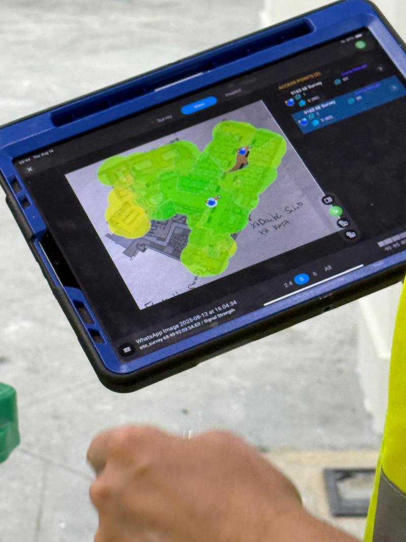 A tablet showing a live Ekahau signal strength heatmap over a floorplan, coverage shaded green and yellow