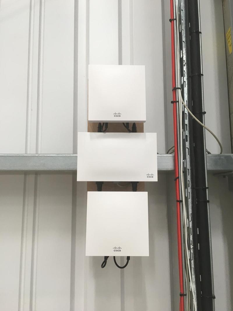 Three access points mounted one above another on timber backboards fixed to a profiled steel wall in an industrial unit, containment running down beside them