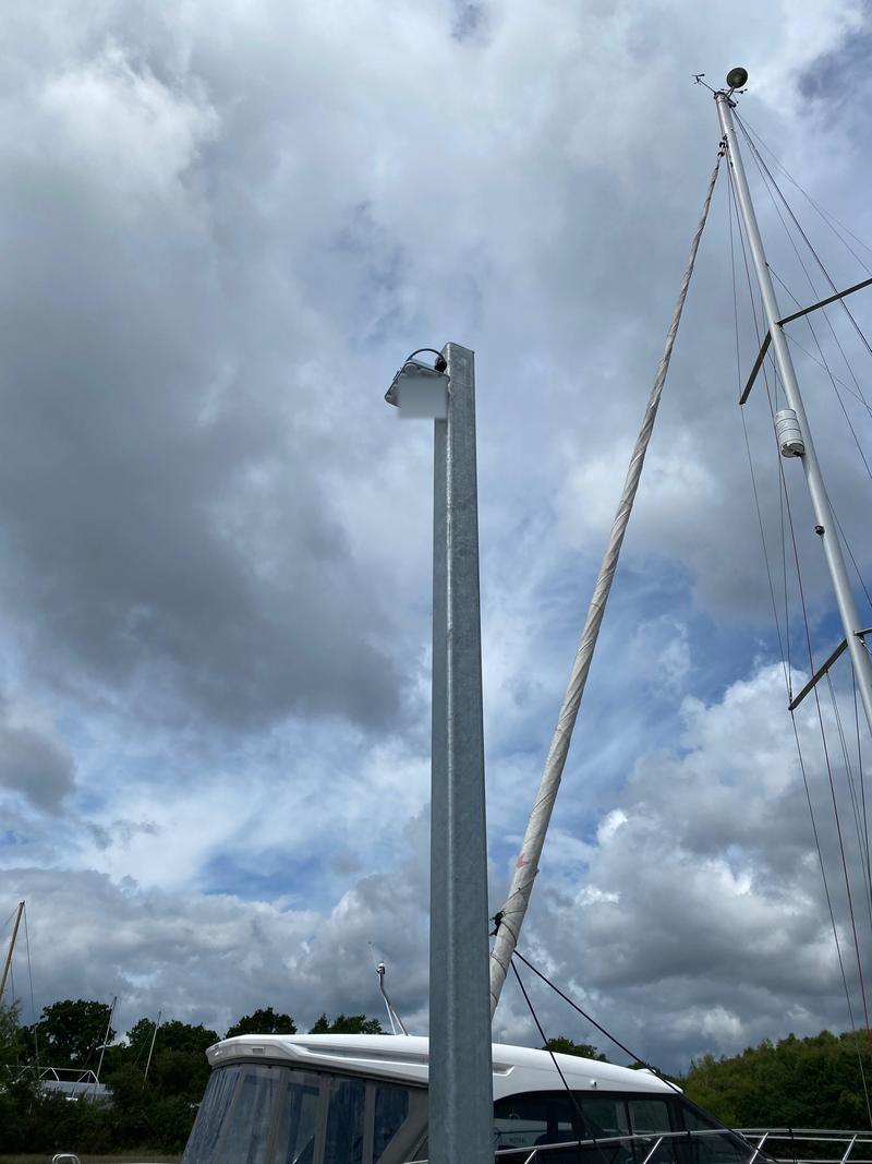 An access point on a galvanised post against cloud, with a yacht mast alongside