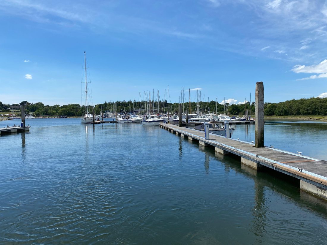 The marina at Beaulieu, timber pontoons running out between rows of moored yachts towards a wooded shore