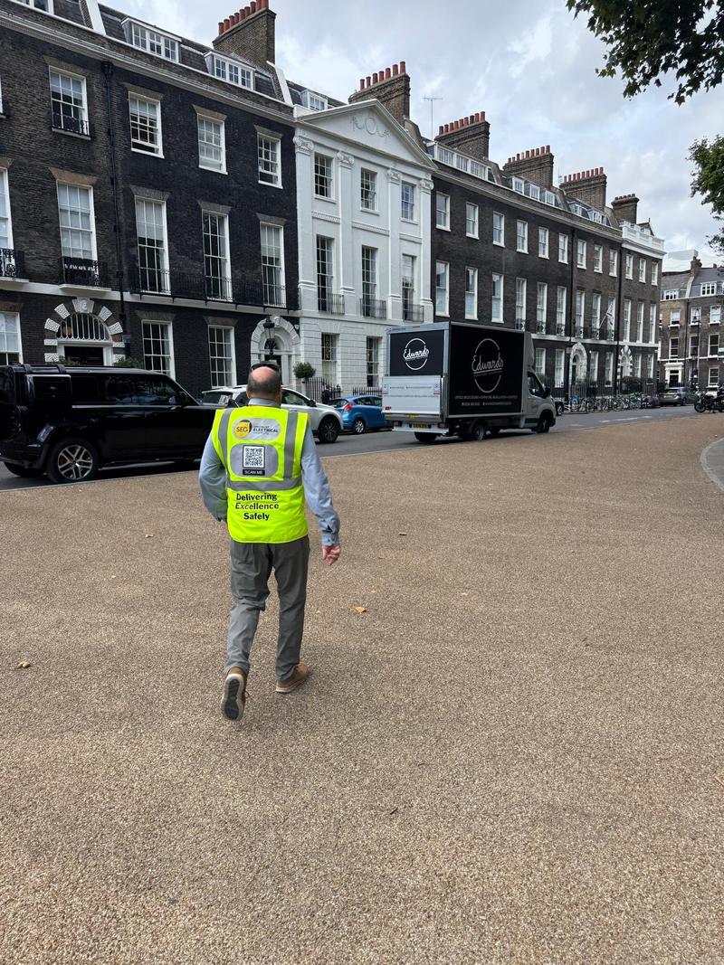 A SEGwifi engineer in branded hi-vis walking across a London square towards a Georgian terrace