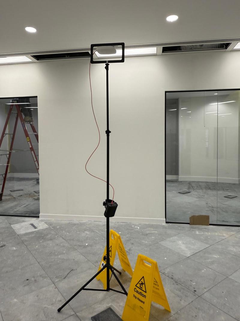 A survey tripod carrying an access point at ceiling height in an open-plan office with glass partitions behind it